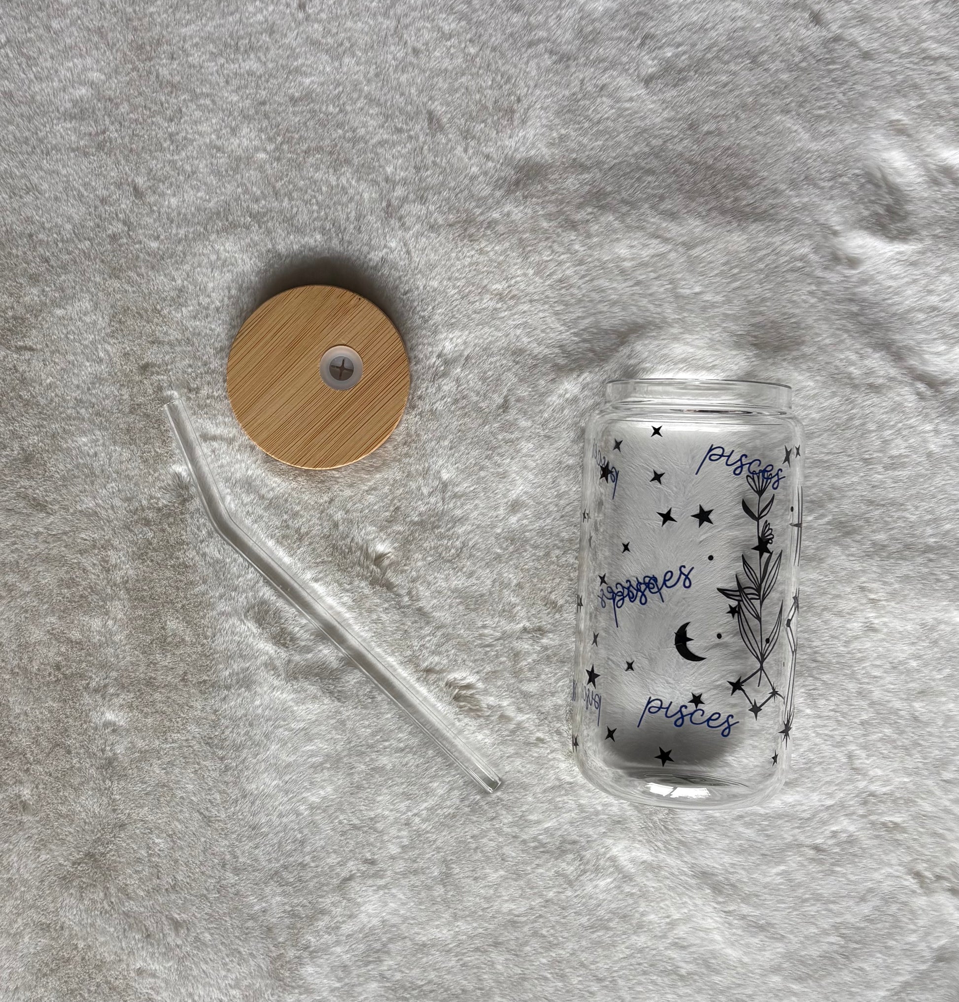 Glass can cup with glass straw and bamboo lid. Design on the glass cup is the Pisces zodiac symbol, star constellation, flower and the text Pisces on the backside