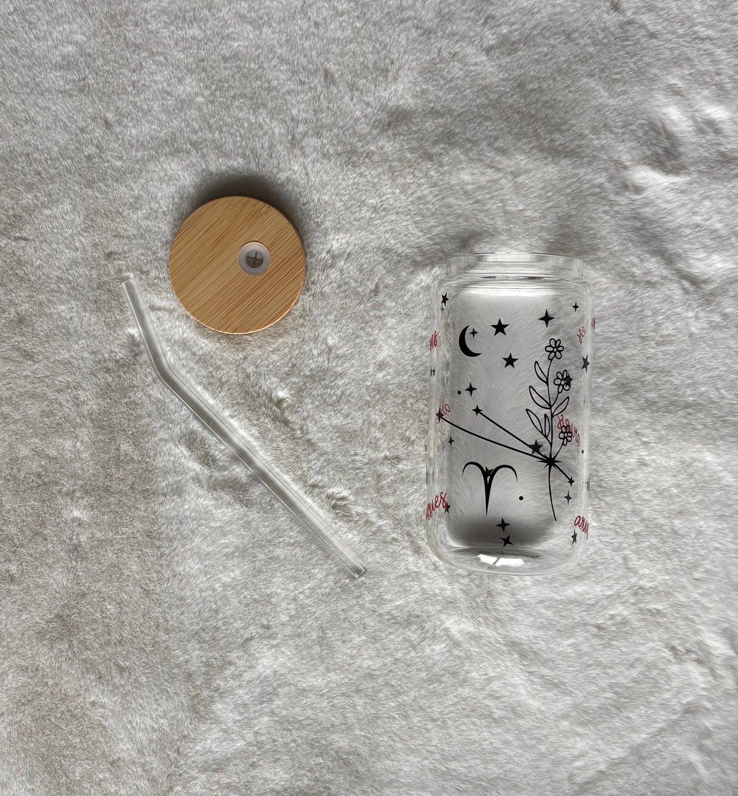 Glass can cup with glass straw and bamboo lid. Design on the glass cup is the Aries zodiac symbol, star constellation, flower and the text Aries on the backside.