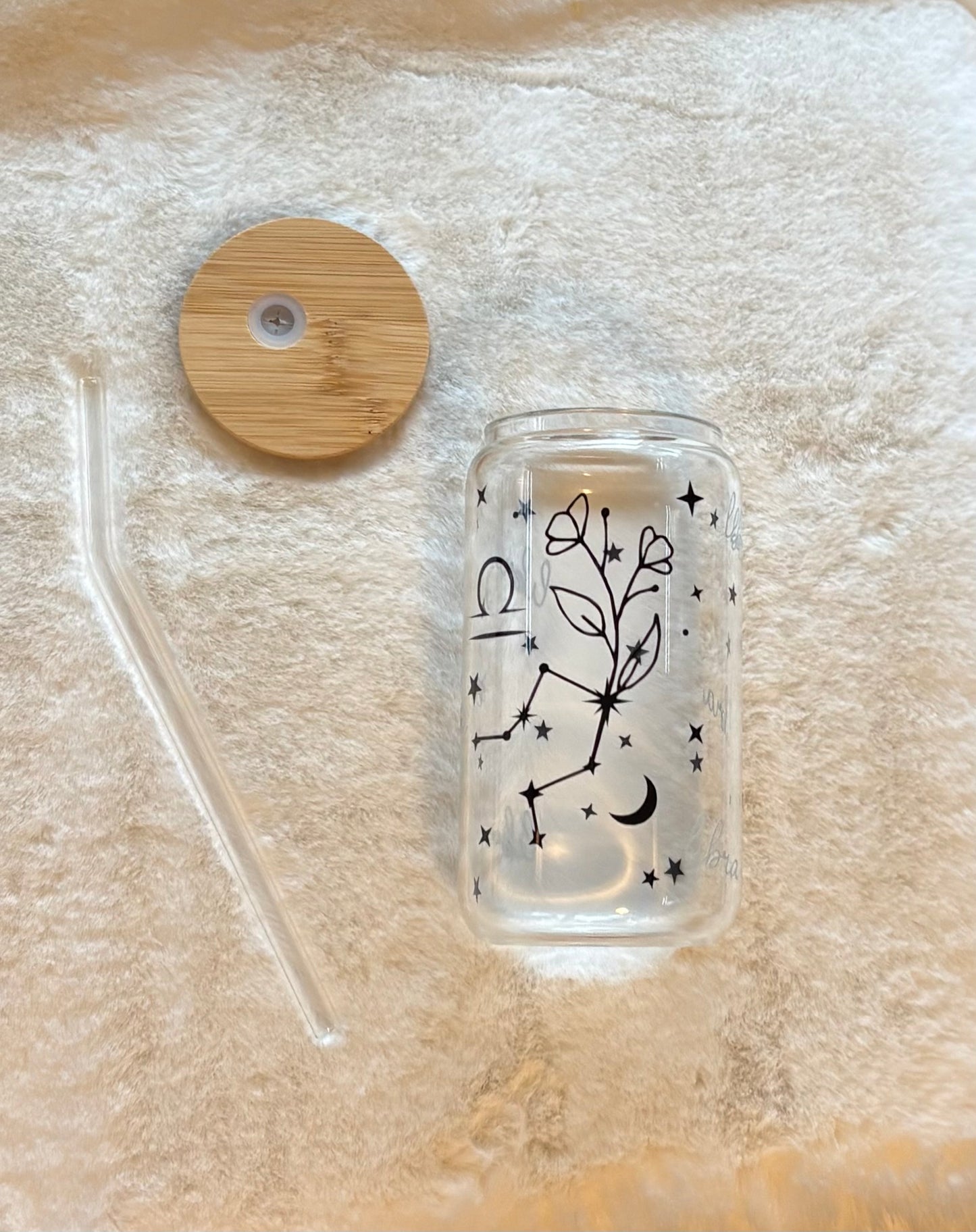 Glass can cup with glass straw and bamboo lid. Design on the glass cup is the Libra zodiac symbol, star constellation, flower and the text Libra on the backside