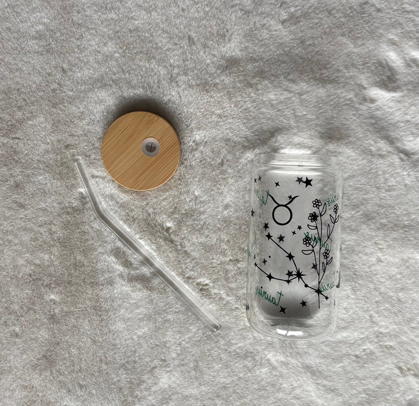Glass can cup with glass straw and bamboo lid. Design on the glass cup is the Taurus zodiac symbol, star constellation, flower and the text Taurus on the backside