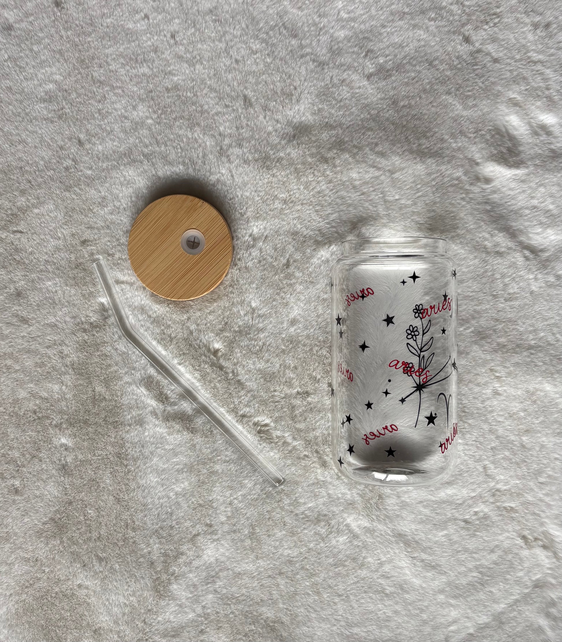 Glass can cup with glass straw and bamboo lid. Design on the glass cup is the Aries zodiac symbol, star constellation, flower and the text Aries on the backside