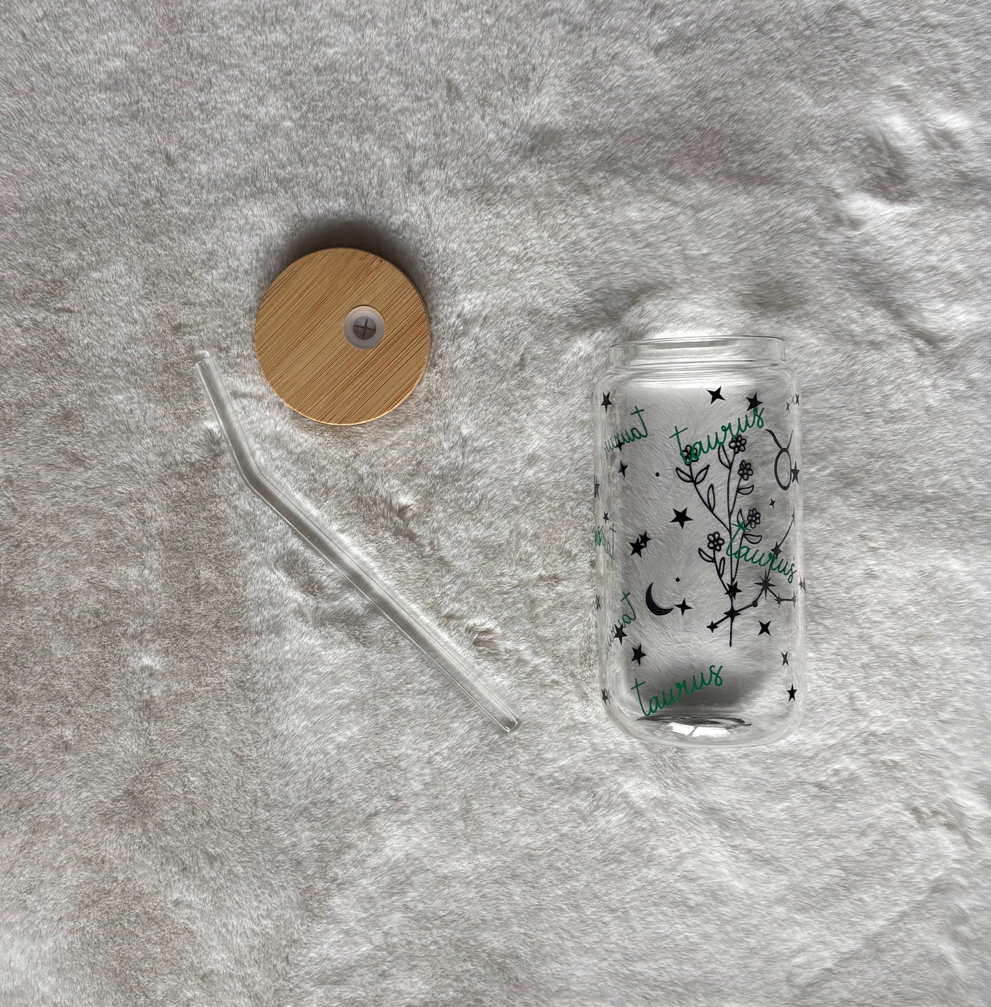 Glass can cup with glass straw and bamboo lid. Design on the glass cup is the Taurus zodiac symbol, star constellation, flower and the text Taurus on the backside